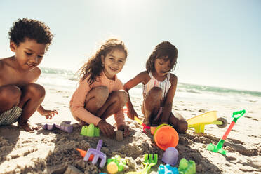 Eine Gruppe glücklicher Kinder, die mit ihren Spielsachen am Strand spielen. Drei sorglose Kinder, die sich in den Sommerferien an einem sonnigen Strand amüsieren. - JLPSF09980