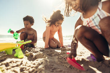 Drei neugierige junge Freunde spielen mit ihren Spielsachen am Strand. Eine Gruppe glücklicher Kinder, die sich in den Sommerferien an einem sonnigen Strand vergnügen. - JLPSF09981