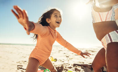 Fröhliches kleines Mädchen, das mit seinen Freunden am Strand spielt. Entzückendes junges Mädchen, das mit ausgestreckten Armen fröhlich lacht. Unbekümmerte Kinder, die sich in den Sommerferien vergnügen. - JLPSF09982