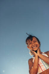Fröhliches kleines Mädchen, das sich in den Sommerferien am Strand vergnügt. Ein bezauberndes junges Mädchen, das in die Kamera lächelt, während es mit dem Himmel im Hintergrund steht. - JLPSF09985
