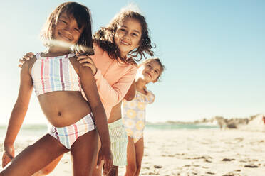 Drei aktive junge Mädchen, die zusammen am Strand spielen und Spaß haben. Eine Gruppe glücklicher kleiner Kinder, die ihren Sommerurlaub an einem sonnigen Strand genießen. - JLPSF09989