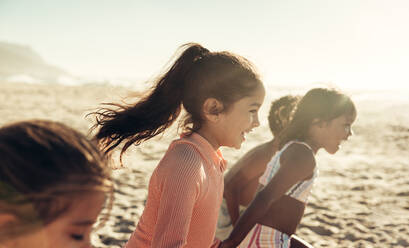 Eine Gruppe energiegeladener Kinder, die gemeinsam am Strand rennen und Spaß haben. Glückliche kleine Kinder, die ihren Sommerurlaub an einem sonnigen Strand genießen. - JLPSF09995