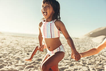 Fröhliches kleines Mädchen, das mit seinen Freunden am Strand entlang rennt und Spaß hat. Eine Gruppe glücklicher kleiner Kinder, die ihren Sommerurlaub an einem sonnigen Strand genießen. - JLPSF09997