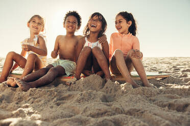 Glücksgefühle am Strand. Liebenswerte kleine Kinder lachen fröhlich, während sie zusammen am Strand sitzen. Eine Gruppe unbeschwerter junger Freunde, die in den Sommerferien zusammen Spaß haben. - JLPSF10002