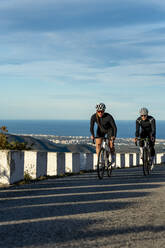 Sportlerin im Wettstreit mit einem Sportler beim Radfahren auf einem Bergpass an der Costa Blanca in Alicante, Spanien - AMNF00005