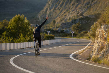 Radfahrer mit erhobener Hand auf der Straße am Costa-Blanca-Pass in Alicante, Spanien - AMNF00015