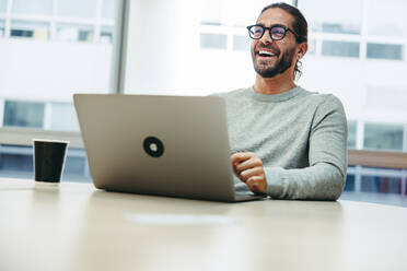 Fröhlicher junger Geschäftsmann, der fröhlich lacht, während er mit einem Laptop arbeitet. Erfolgreicher Unternehmer, der aus der Ferne in einem Co-Working Space arbeitet. - JLPSF10120