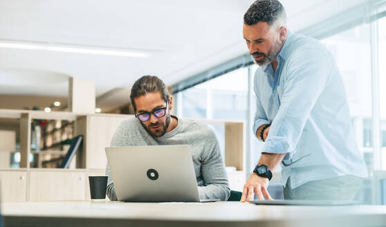 Geschäftsleute, die in einem modernen Co-Working-Büro zusammenarbeiten und dabei eine Diskussion führen. Zwei konzentrierte Geschäftsleute, die einen Laptop benutzen, während sie ein neues Projekt planen. - JLPSF10123