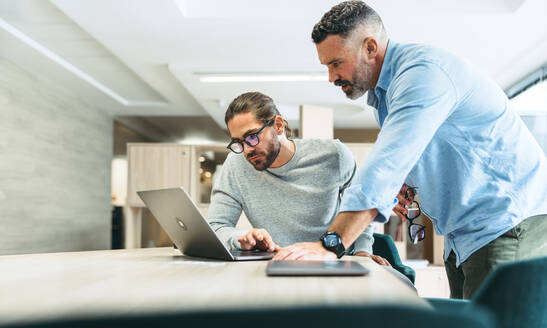 Moderne Geschäftsleute führen eine wichtige Diskussion, während sie in einem Co-Working-Büro zusammenarbeiten. Zwei konzentrierte Geschäftsleute arbeiten mit einem Laptop an einem neuen Projekt. - JLPSF10125