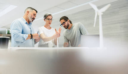 Innovative designers working with 3D wind turbine models in a modern office. Group of creative businesspeople having a discussion while working on a renewable energy project. - JLPSF10129