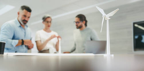 Creative design professionals working with 3D wind turbine models in a modern office. Group of innovative businesspeople brainstorming while working on a renewable energy project. - JLPSF10130
