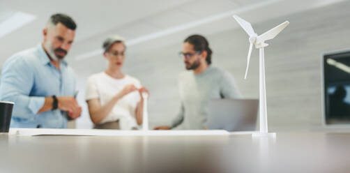 Kreative Designer, die in einem modernen Büro mit 3D-Windturbinenmodellen arbeiten. Eine Gruppe innovativer Geschäftsleute beim Brainstorming, während sie an einem Projekt für erneuerbare Energien arbeiten. - JLPSF10130