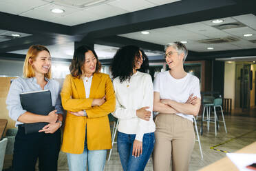 Multikulturelle Geschäftsfrauen lachen fröhlich, während sie in einem Co-Working-Büro stehen. Gruppe von fröhlichen Geschäftsfrauen, die als Team zusammenarbeiten. - JLPSF10147