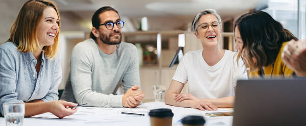 Fröhlich lächelnde Design-Profis bei einer Besprechung in einem modernen Büro. Eine Gruppe innovativer Geschäftsleute tauscht kreative Ideen aus, während sie an einem neuen Projekt arbeiten. - JLPSF10157