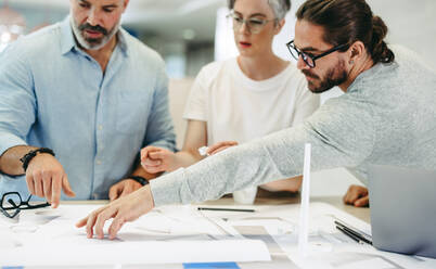 Innovative designers working with wind turbine blueprints in a modern office. Group of creative businesspeople having a discussion while working on a renewable energy project. - JLPSF10198