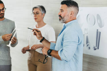 Mature design professional leading a discussion during a meeting with his colleagues. Creative businesspeople sharing innovative ideas while working on a wind turbine project. - JLPSF10204