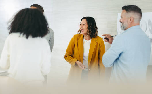 Fröhliche Geschäftsleute lachen fröhlich, während sie sich über ein kreatives Büro unterhalten. Eine Gruppe multikultureller Design-Profis arbeitet gemeinsam an einem neuen innovativen Projekt. - JLPSF10207
