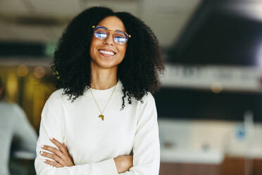 Confident young businesswoman smiling at the camera while standing with her arms crossed. Happy black businesswoman working remotely in a co-working space. - JLPSF10215