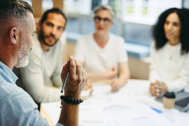 Ein reifer Geschäftsmann diskutiert mit seinem Team während einer Besprechung. Eine Gruppe innovativer Design-Profis tauscht kreative Ideen aus, während sie an einem neuen Projekt arbeiten. - JLPSF10219