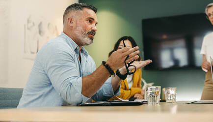 Mature businessman having a discussion with his colleagues in a modern workplace. Experienced entrepreneur sharing creative ideas with his team during a boardroom meeting. - JLPSF10233