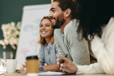 Young businessman attending a meeting with his team. Group of cheerful businesspeople having a discussion while sitting together in a boardroom. - JLPSF10242