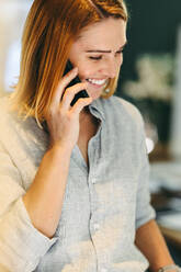 Glückliche junge Geschäftsfrau, die fröhlich lächelt, während sie ein Telefongespräch führt. Erfolgreiche Geschäftsfrau, die mit ihren Geschäftspartnern in einem modernen Büro kommuniziert. - JLPSF10249