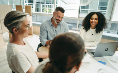 Happy businesspeople smiling cheerfully during a meeting in a modern office. Group of innovative businesspeople working with blueprints. Team of creative engineers planning a new project. - JLPSF10252