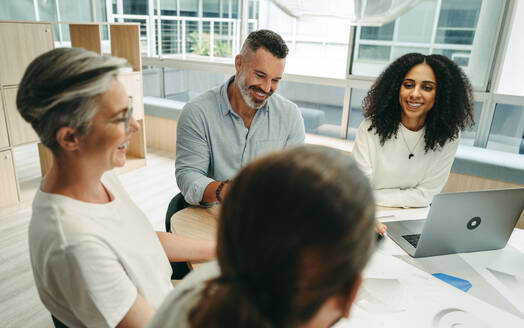 Glückliche Geschäftsleute, die während einer Besprechung in einem modernen Büro fröhlich lächeln. Gruppe innovativer Geschäftsleute, die mit Entwürfen arbeiten. Team kreativer Ingenieure, die ein neues Projekt planen. - JLPSF10252