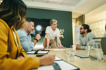 Eine reife Geschäftsfrau führt eine Diskussion mit ihrem Team in einem Sitzungssaal. Eine Gruppe von kreativen Geschäftsleuten tauscht während einer Sitzung an einem modernen Arbeitsplatz Ideen aus. - JLPSF10268
