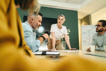 Eine Unternehmerin führt eine Diskussion mit ihren Geschäftskollegen in einem Sitzungssaal. Eine Gruppe von kreativen Geschäftsleuten tauscht während einer Sitzung an einem modernen Arbeitsplatz Ideen aus. - JLPSF10270