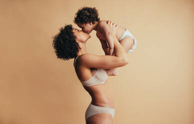 Woman holding up her child and kissing on mothers day. Mother loving her baby. - JLPSF10273