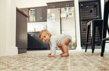 Cute baby trying to stand on his feet. Developing child standing up on floor at home. - JLPSF10321