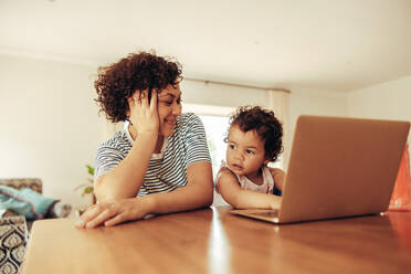 Frau, die eine Arbeitspause macht und ihr Baby am Laptop beobachtet. Mutter und Kind sitzen am Tisch mit einem Laptop. - JLPSF10324
