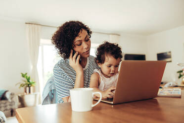 Eine Frau telefoniert mit ihrem Baby, das am Tisch sitzt. Eine berufstätige Mutter spricht mit ihrem Baby zu Hause am Handy. - JLPSF10325