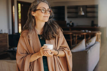 Ältere Frau mit einer Tasse Tee in der Hand, die nachdenklich in die Ferne blickt. Reife Frau, die zu Hause einen ruhigen Lebensabend genießt. - JLPSF10333