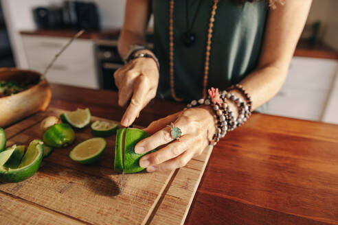 Vegetarian senior woman cutting some limes for green juice in her kitchen. Mature woman preparing a healthy plant-based meal at home. Woman taking care of her aging body with an organic diet. - JLPSF10359