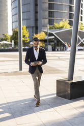 Businessman using smart phone walking on footpath - JCCMF07514