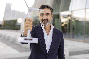 Happy businessman showing wind turbine model - JCCMF07530