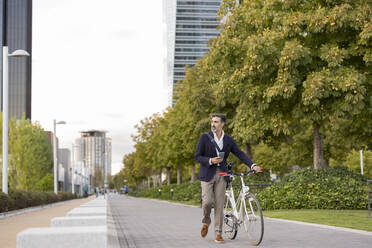 Businessman wheeling with bicycle on footpath - JCCMF07540