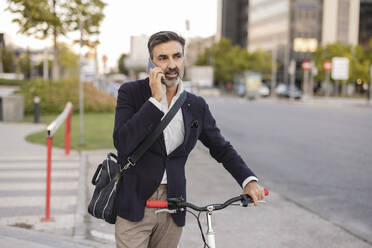 Businessman talking on smart phone with bicycle at roadside - JCCMF07545