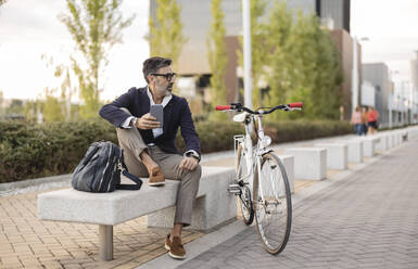 Geschäftsmann mit Smartphone sitzt auf einer Bank am Fahrrad - JCCMF07547
