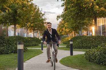 Happy commuter riding bicycle on footpath in park - JCCMF07554