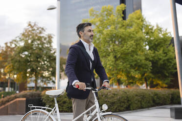 Mature businessman wheeling with bicycle - JCCMF07555