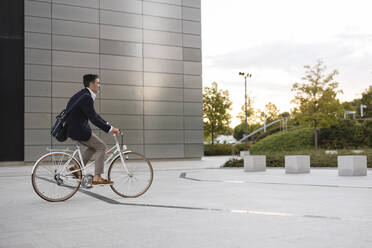 Businessman riding bicycle in front of office building - JCCMF07558
