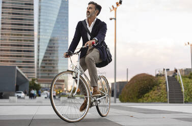 Businessman enjoying riding bicycle on footpath - JCCMF07562