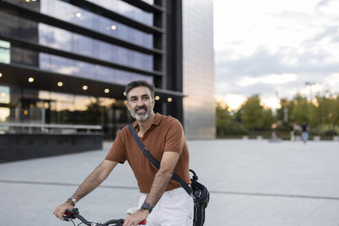 Nachdenklicher Geschäftsmann mit Fahrrad vor einem Bürogebäude - JCCMF07566