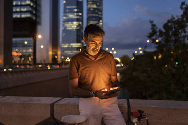 Businessman using smart phone by wall in city at night - JCCMF07608