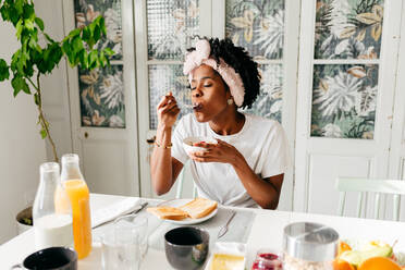 Young black woman with closed eyes enjoying tasty dish while sitting at table and having breakfast in morning at home - ADSF39418