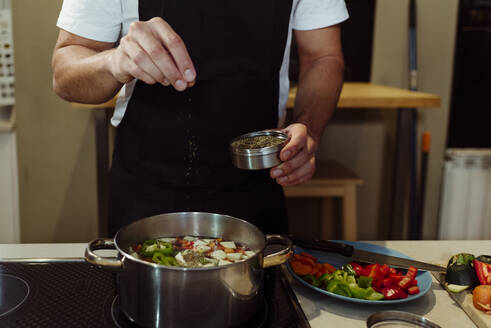 Cropped unerkennbar männlichen Koch mit Schürze Kochen Gemüse in der Pfanne auf dem Herd in der Küche zu Hause - ADSF39454