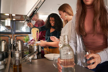 Inhalt junge multiethnische Freundinnen in Freizeitkleidung, die leckere Spaghetti auf einen Teller in der Nähe der Theke eines modernen Selbstbedienungsrestaurants legen - ADSF39472